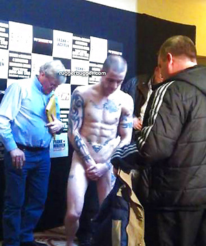The heavily tattooed tough guy demurely stands on the scales covering his cock and balls